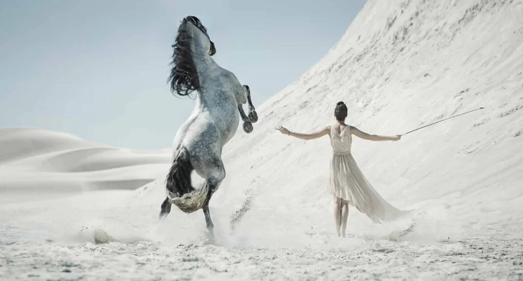 woman and horse dancing on white sand