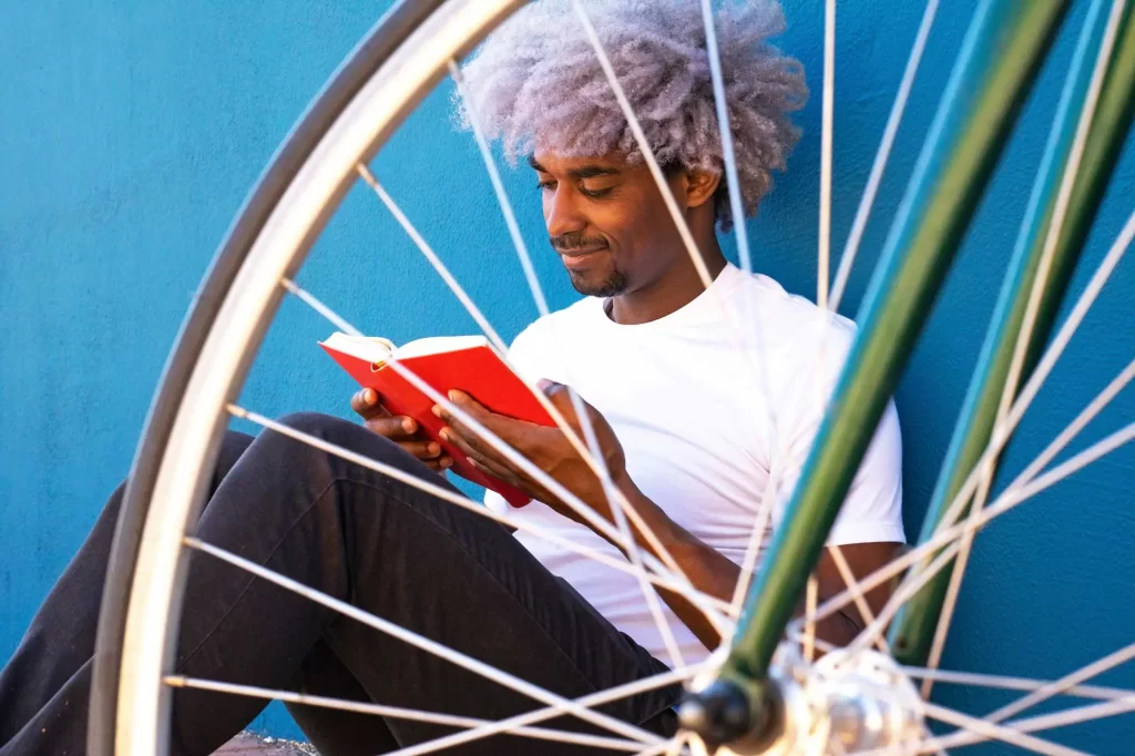 young man reading book behind bike wheel offset 1057246